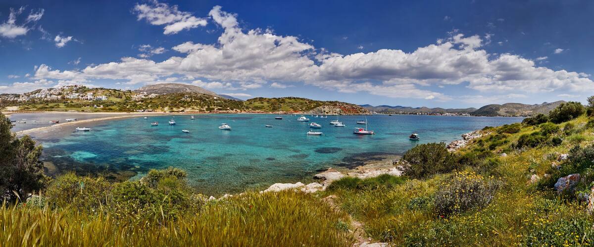 A coastal landscape with clear turquoise waters, boats, and a hillside settlement.