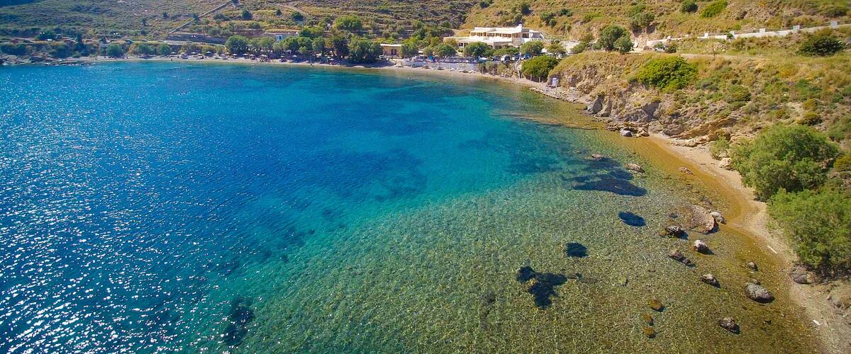 A coastal landscape with clear blue waters, rocky shores, and a hillside with sparse vegetation.