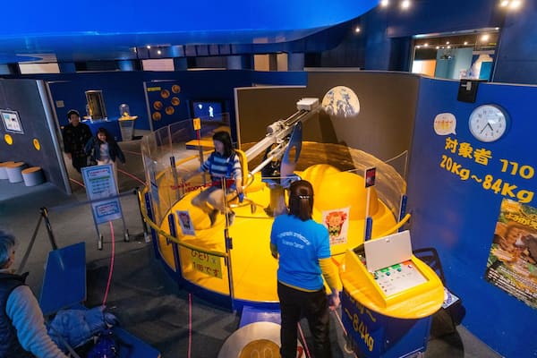 Une exposition sur le thème de l’espace, aux couleurs jaune et bleu, présentant une navette spatiale et une maquette à l’échelle d’une planète.
