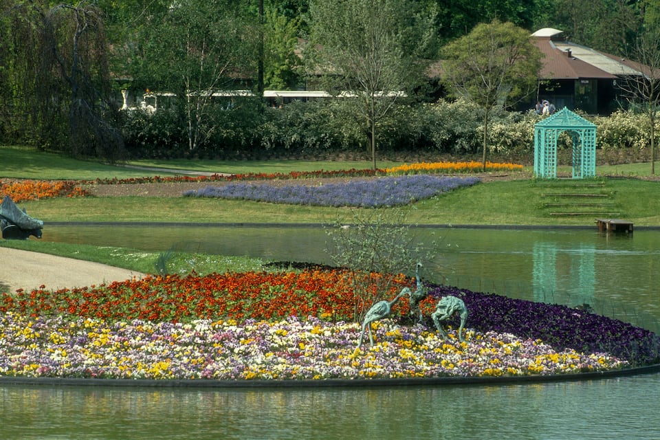A garden with a pond, colorful flower beds, and a gazebo.