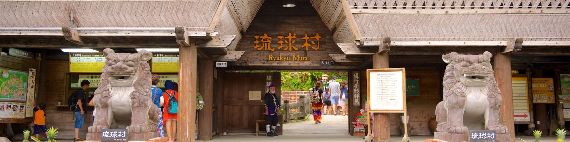 Entrada a Ryukyu Mura con arquitectura tradicional, estatuas de leones de piedra y visitantes.
