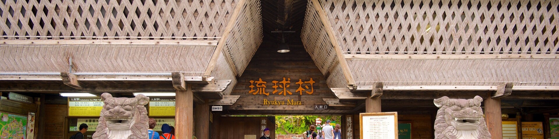 Entrada a Ryukyu Mura con arquitectura tradicional, estatuas de leones de piedra y visitantes.