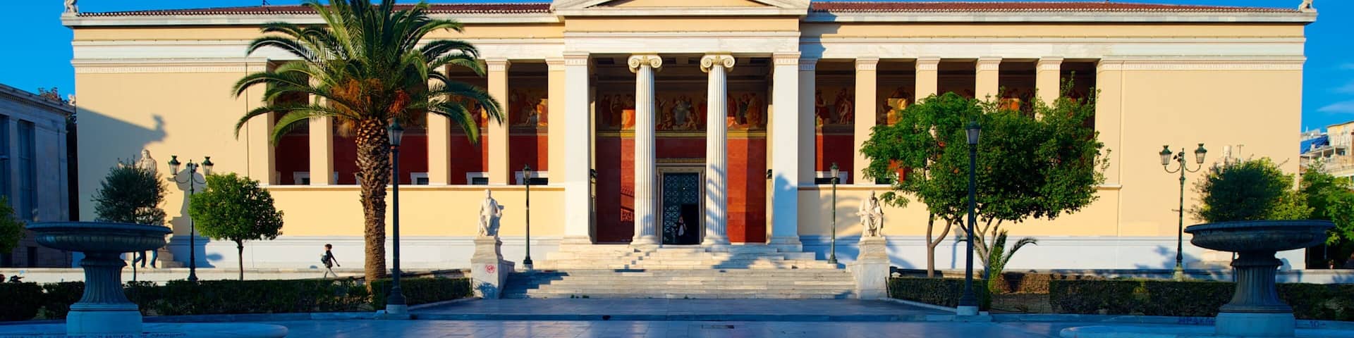 A neoclassical building with columns, a flag, and a statue in front.