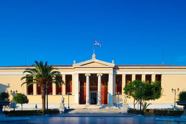 A neoclassical building with columns, a flag, and a statue in front.