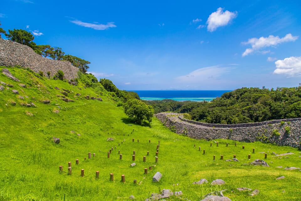 Um declive gramado com um muro de pedra e postes de madeira, com vista para um mar turquesa.