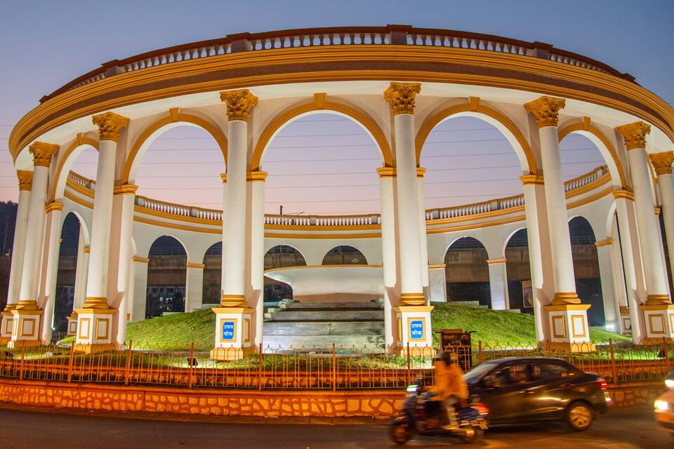 A large, white, circular building with golden accents and multiple arches.