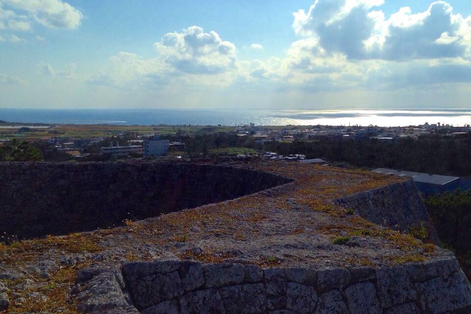 Un paisaje costero con muros de piedra, una vista distante del mar y edificios dispersos.