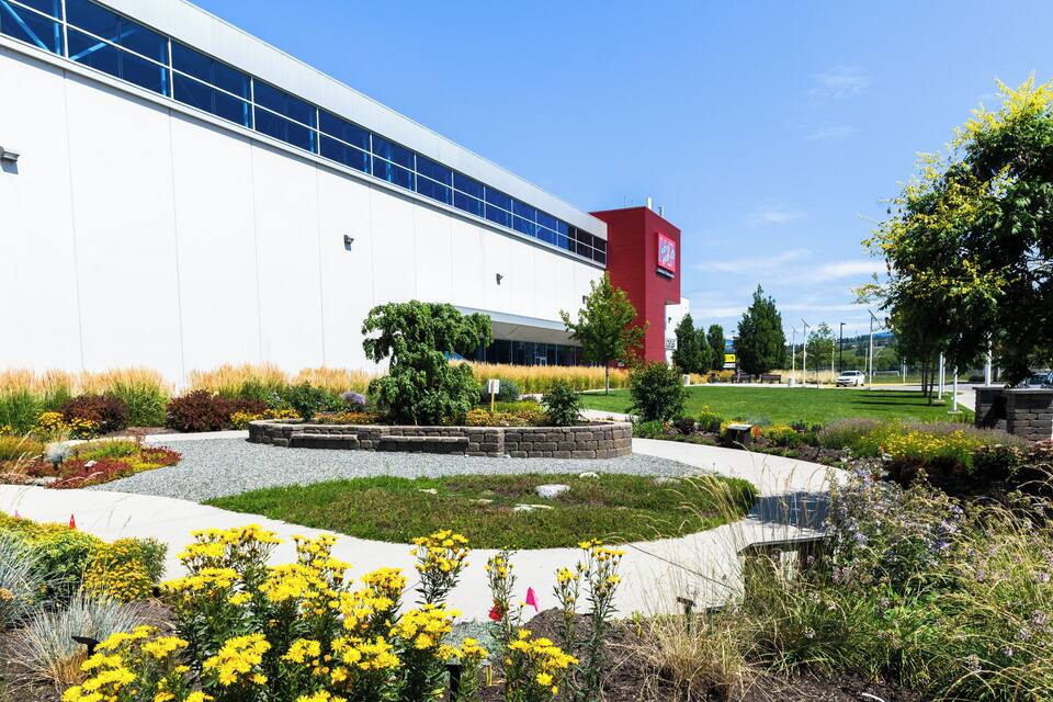 A modern building with a red sign, surrounded by landscaped gardens and a clear blue sky.
