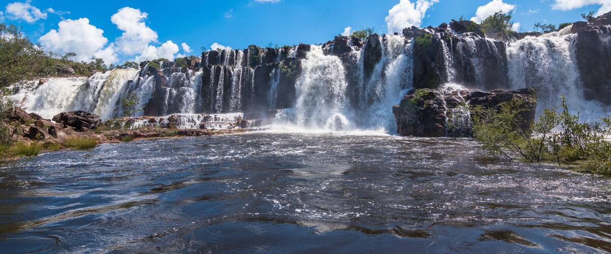 A multi-tiered waterfall cascading over rocky terrain with clear blue skies above.