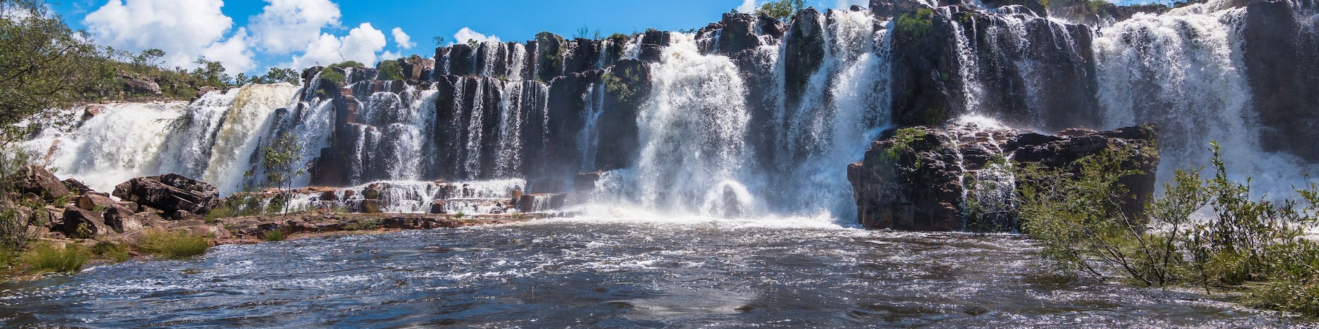 A multi-tiered waterfall cascading over rocky terrain with clear blue skies above.