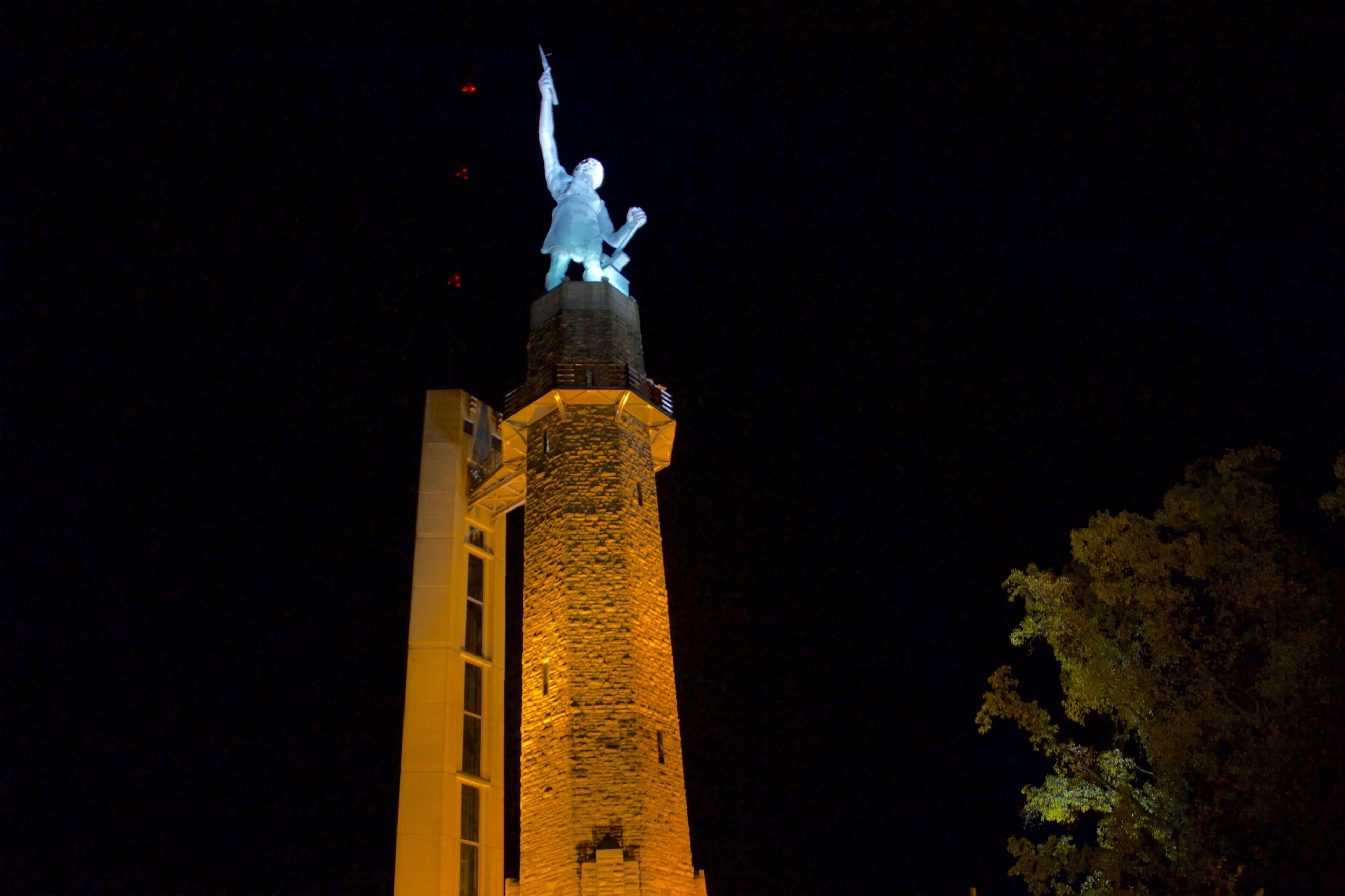 A tower with a statue on top, a brick structure, and a tree in the background.