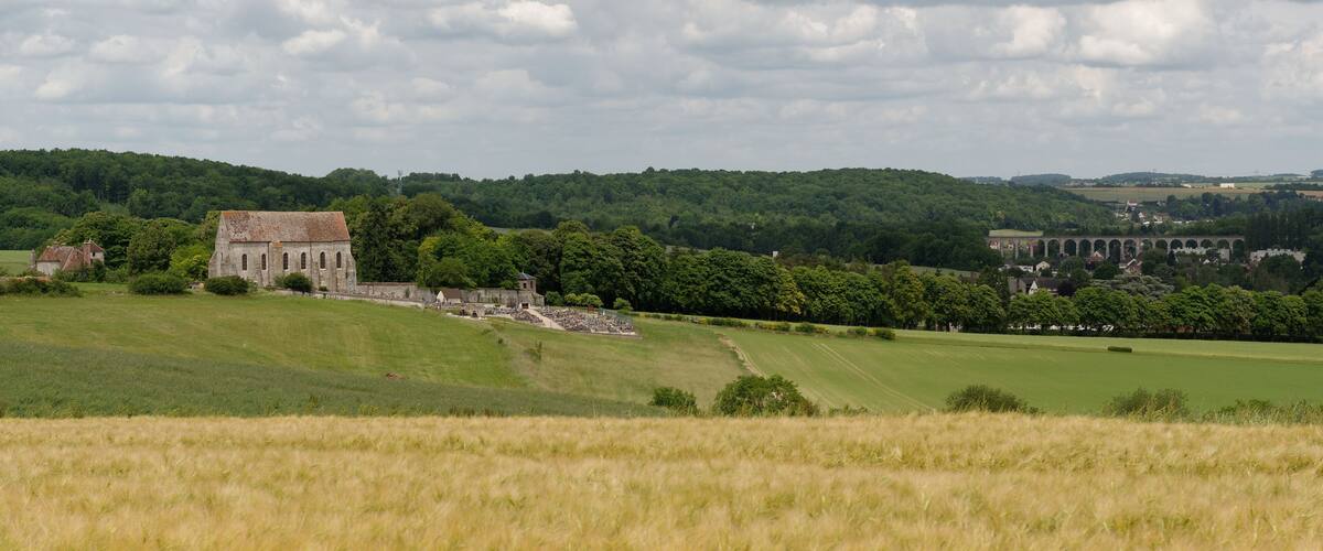 A historic church and ruins in a rural landscape with rolling hills and a cloudy sky.