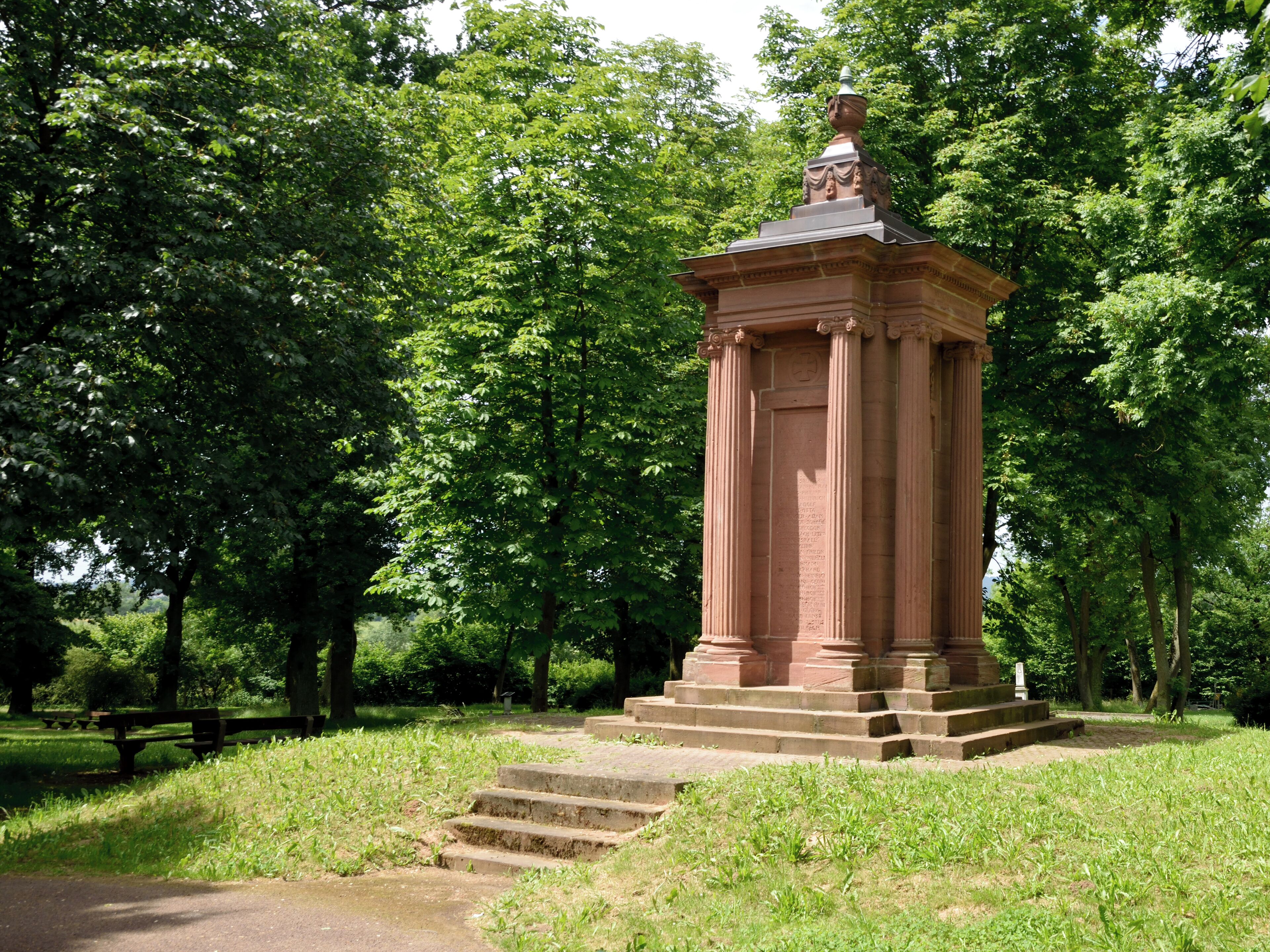 A stone monument with steps in a park surrounded by trees.