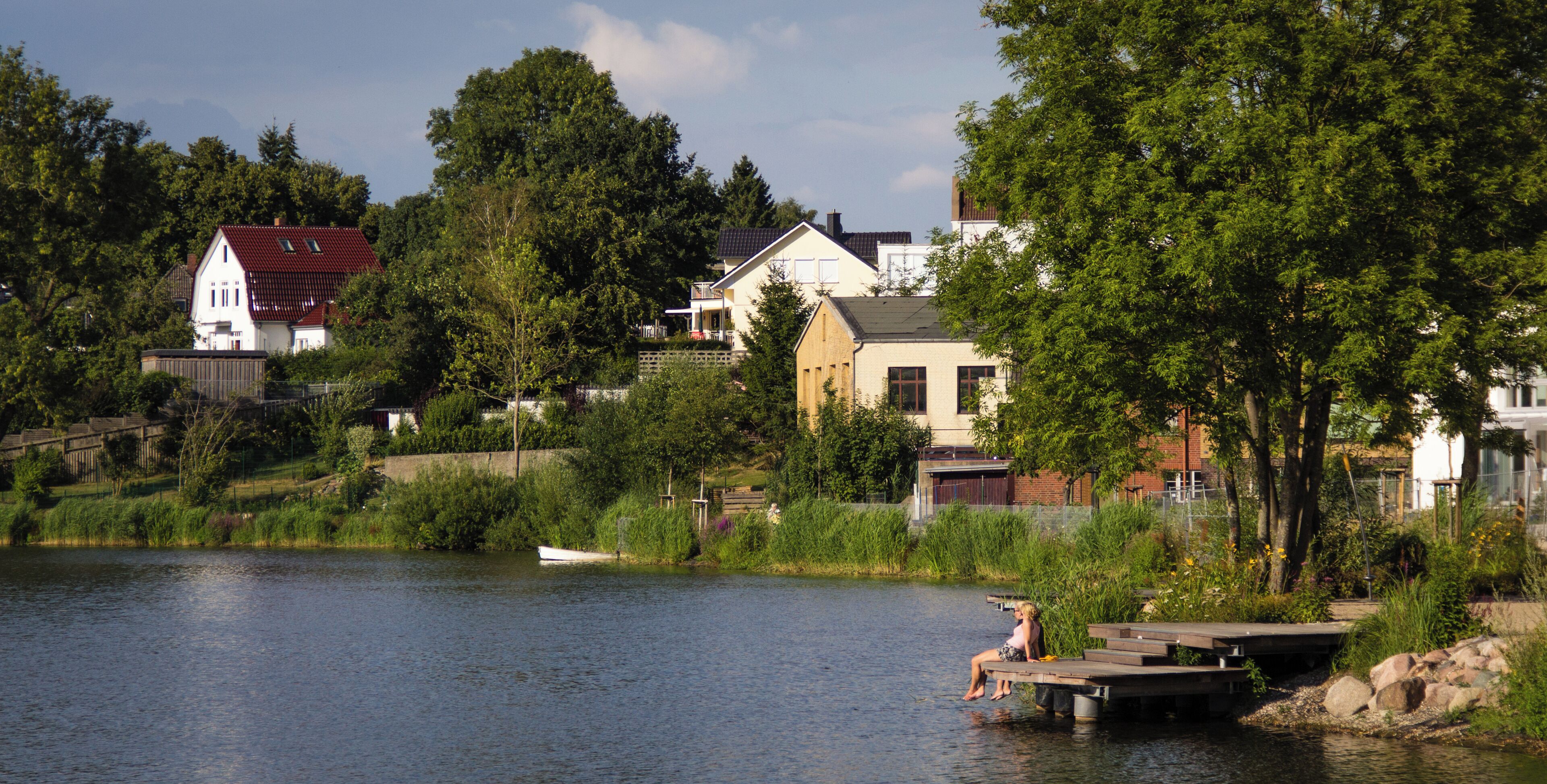 A lake with a dock, a boat, and houses in the background.