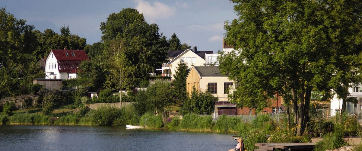 A lake with a dock, a boat, and houses in the background.