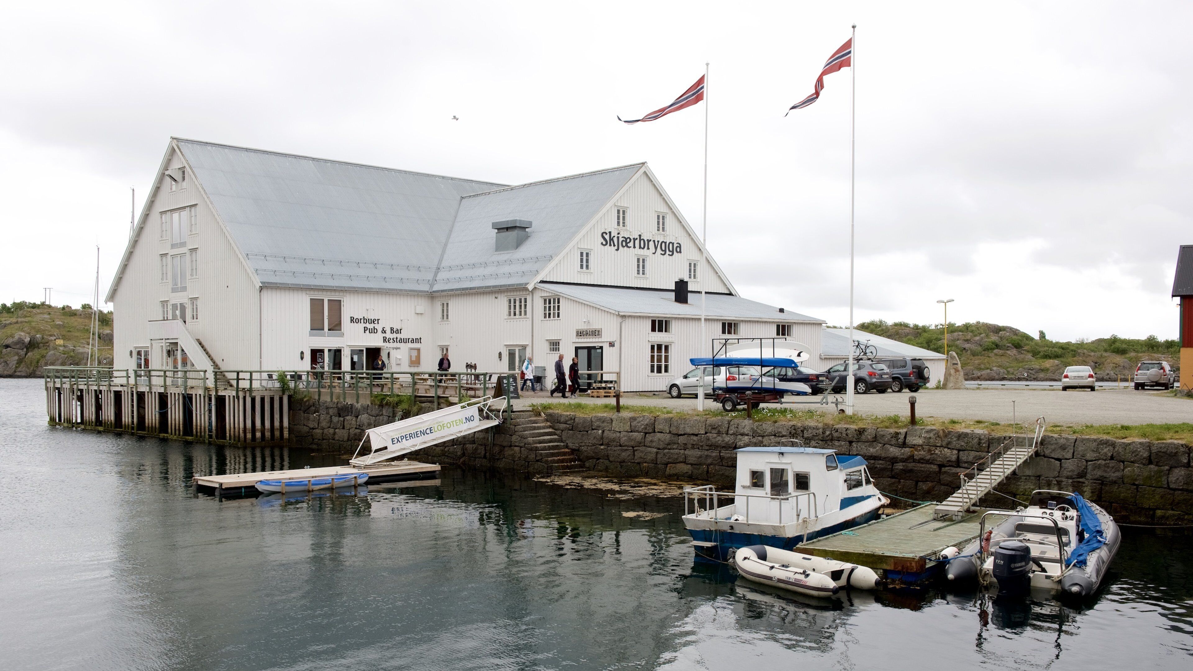 A white building with a sign reading "Skjerbrygga" and a dock with boats.