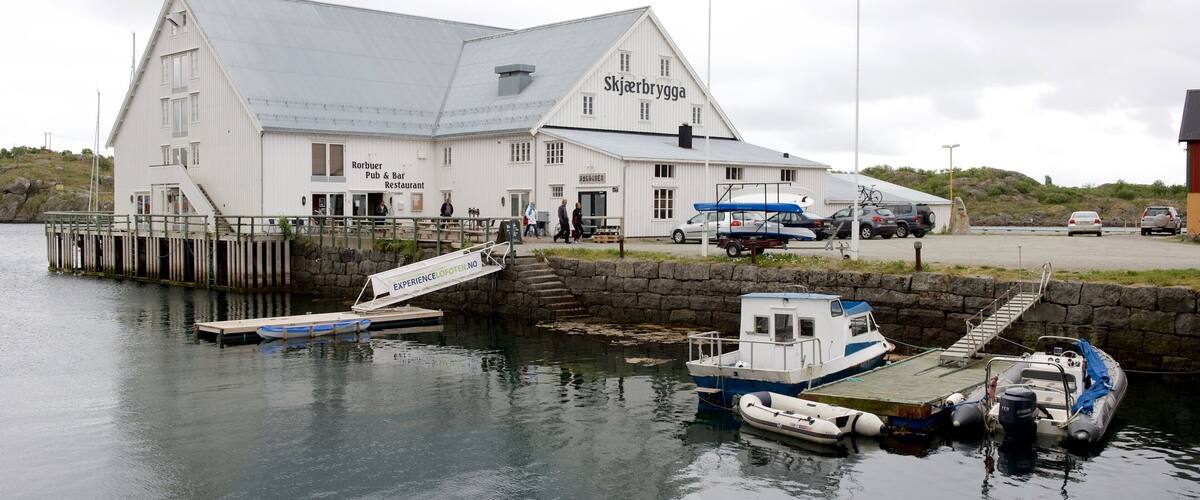 A white building with a sign reading "Skjerbrygga" and a dock with boats.