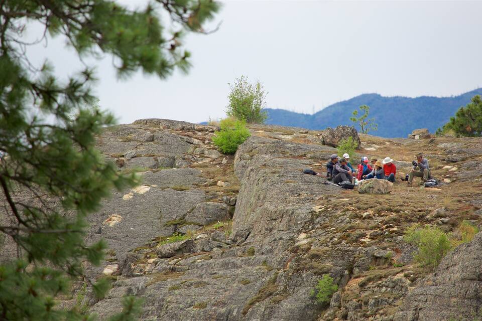 A group of people sitting on a rocky hillside with sparse vegetation and mountains in the background.