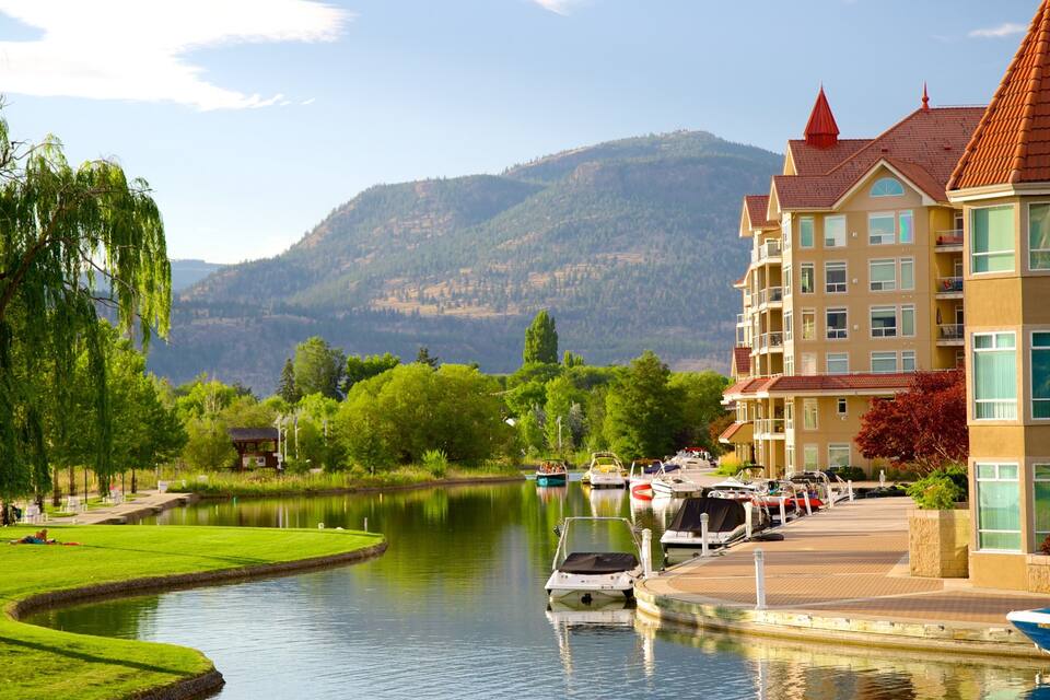 A riverside view with boats, a park, and a building with a red roof.