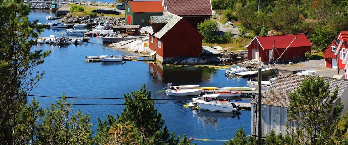 A coastal village with boats docked at a harbor, surrounded by greenery and red buildings.