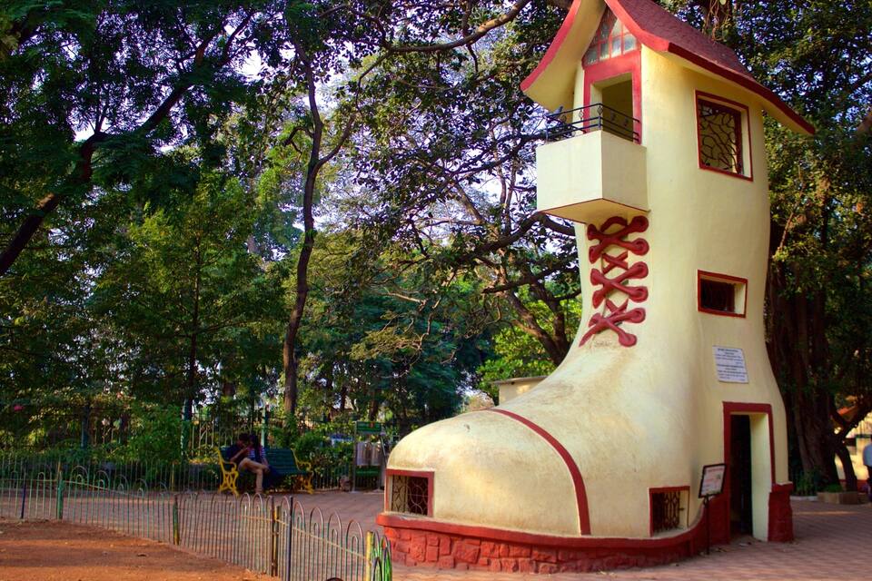 Un edificio grande y de forma peculiar que recuerda a un zapato gigante, con una combinación de colores rojo y amarillo, rodeado de árboles.