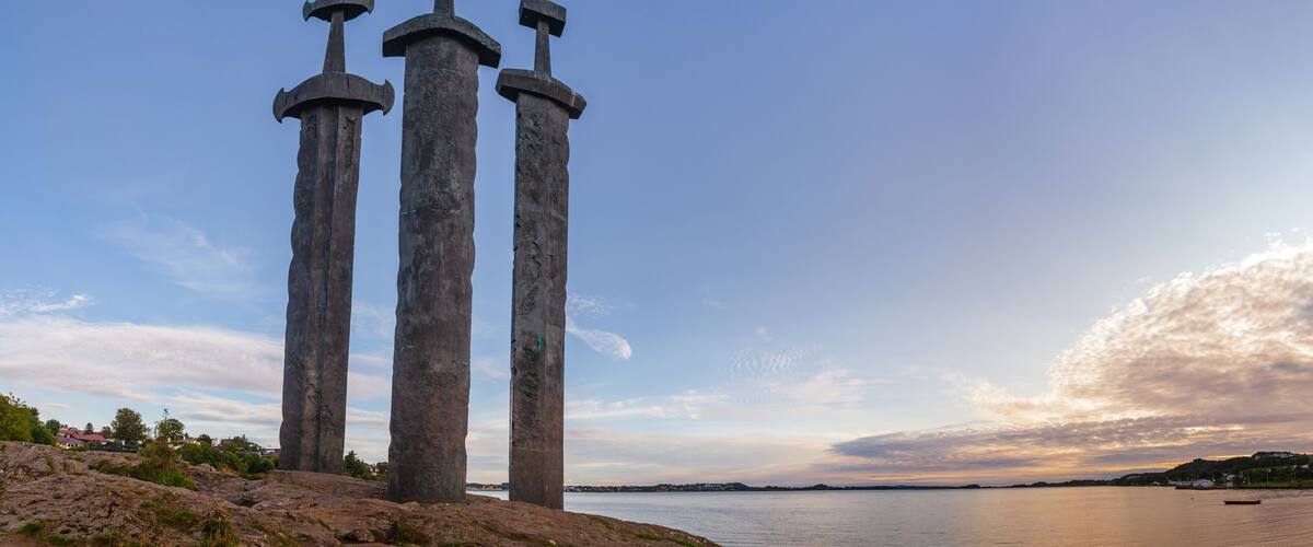Three tall stone pillars with hammer tops by a body of water.