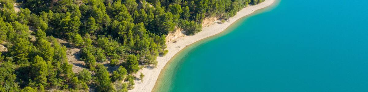 A coastal landscape with a sandy beach, dense green forest, and clear turquoise waters.