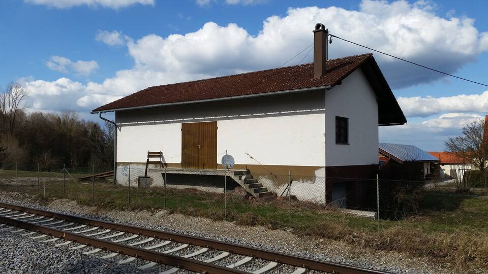A small white building with a brown roof next to railway tracks.