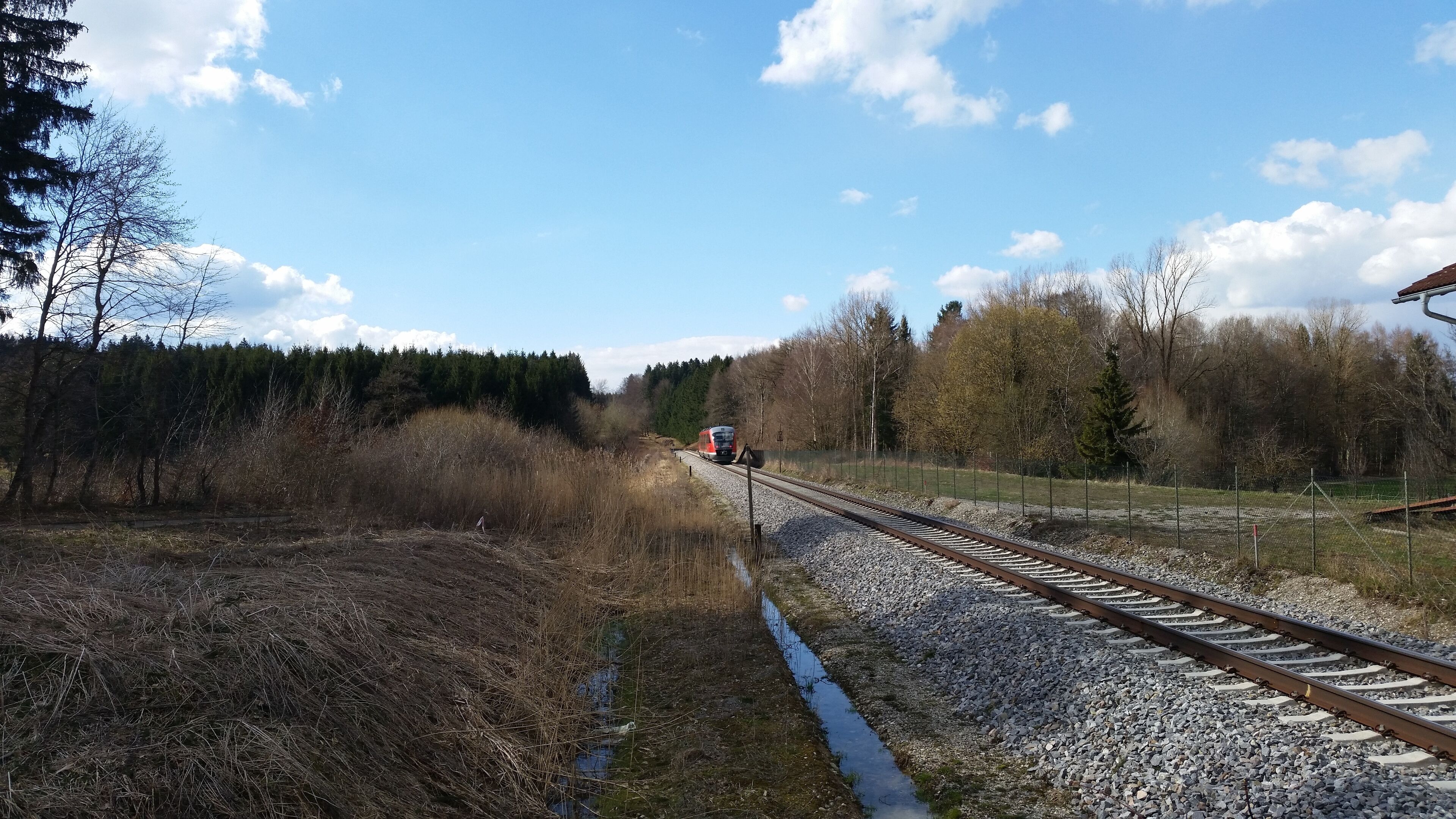 A railway track with a train approaching, surrounded by trees and a clear sky.