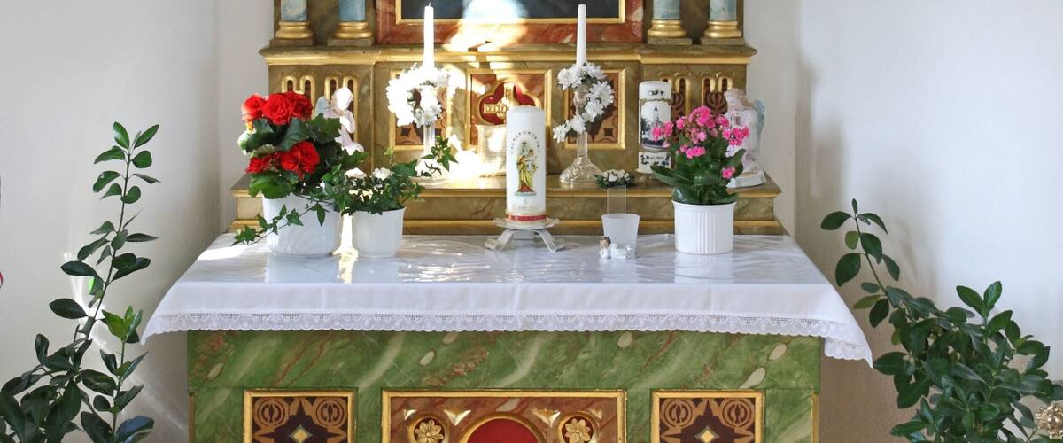 A religious altar with a crucifix, a framed painting, candles, flowers, and a cross on the front.