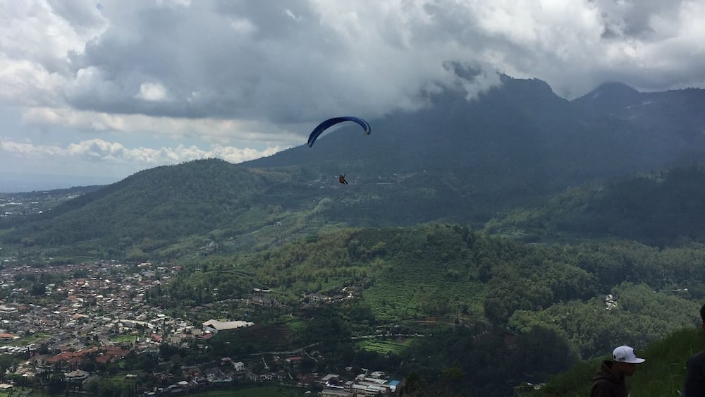 En person paraglider over et bjerglandskab med en landsby nedenfor.