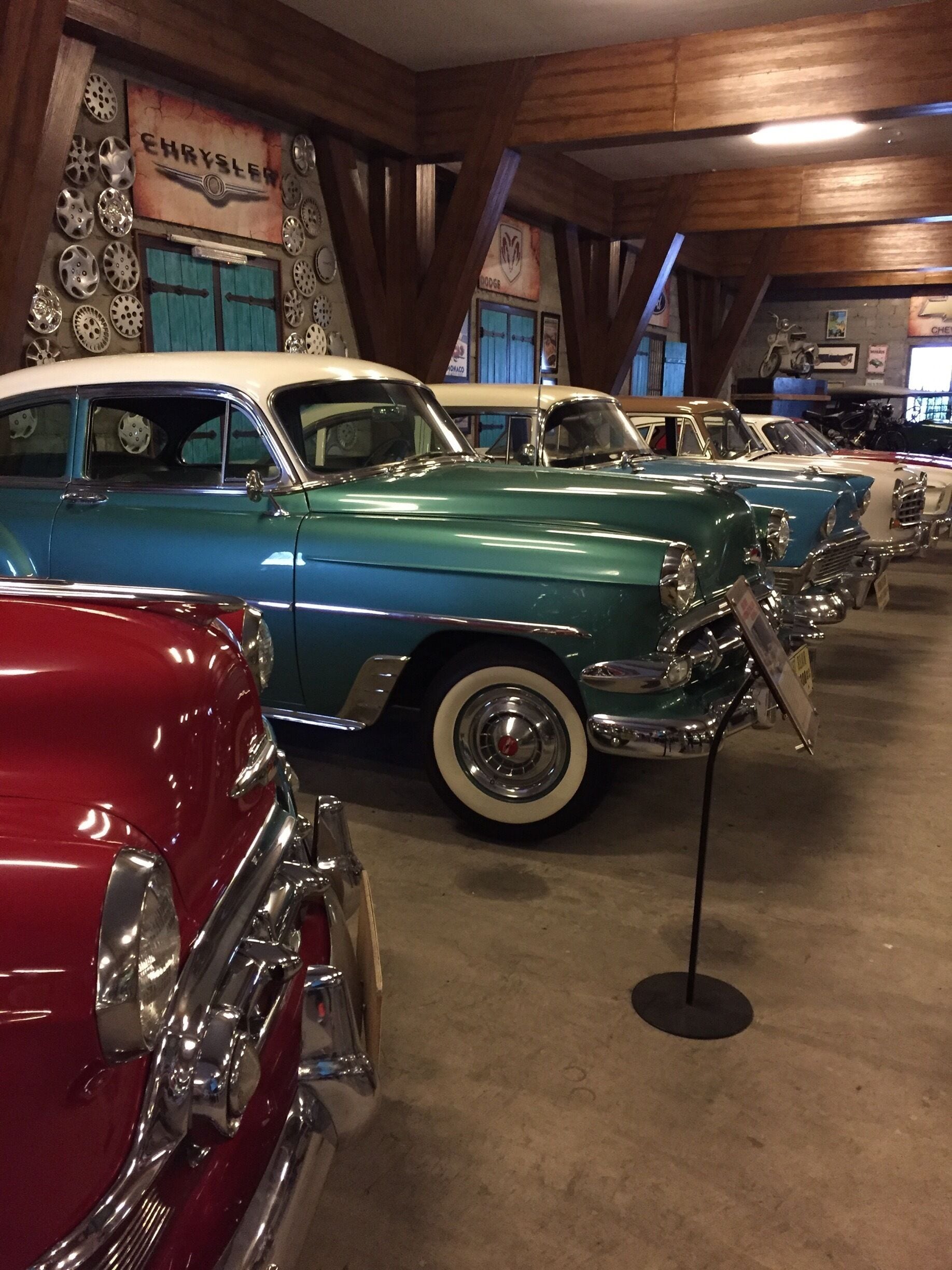 Vintage cars on display in a museum with wooden beams and a Chrysler sign.