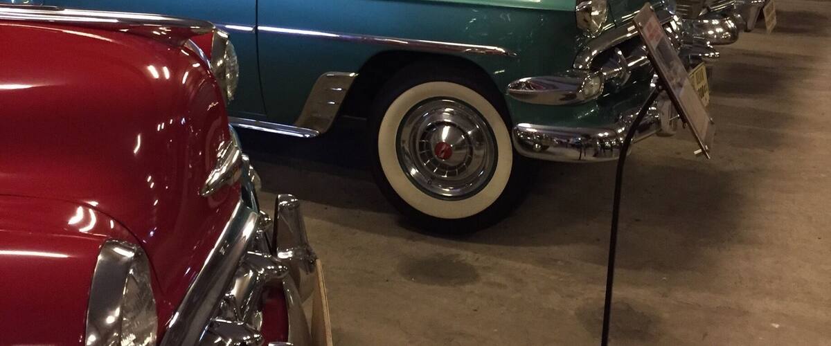 Vintage cars on display in a museum with wooden beams and a Chrysler sign.