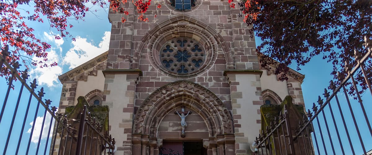 A historic church with a large rose window, arched entrance, and a statue of Jesus Christ.