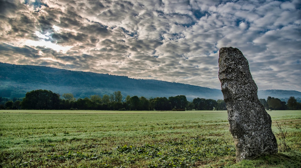 A standing stone in a grassy field with a cloudy sky and a mountain in the background.