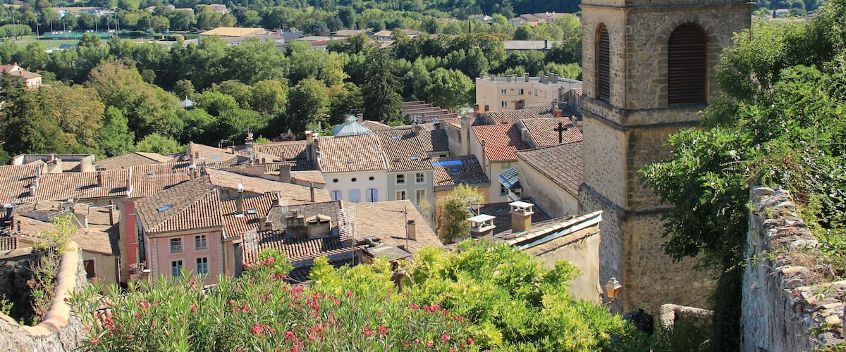 A town with a prominent church tower, lush green hills, and a mountain in the background.
