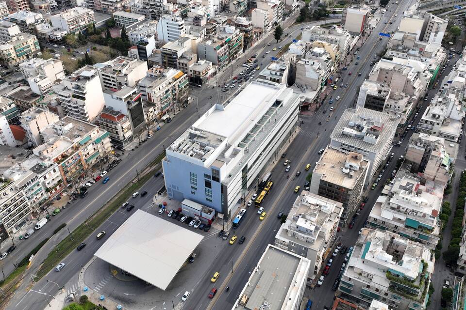 Vista aérea de una ciudad con un edificio azul destacado, una gran estructura blanca y una intersección con mucho tráfico.