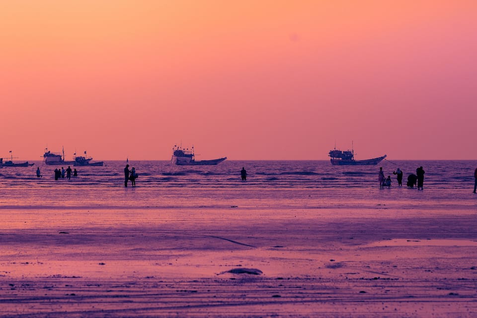 A beach at sunset with boats and people.