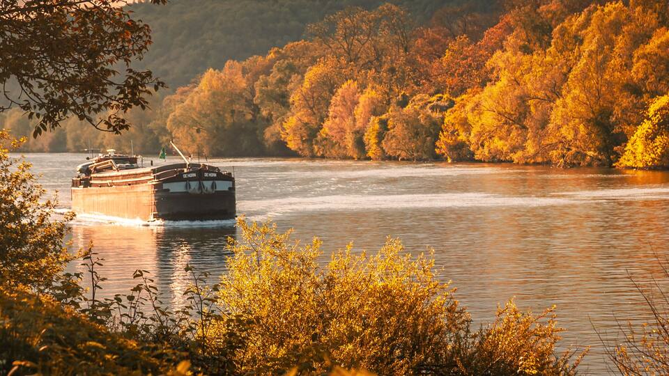 A riverboat on a river surrounded by autumn-colored trees.