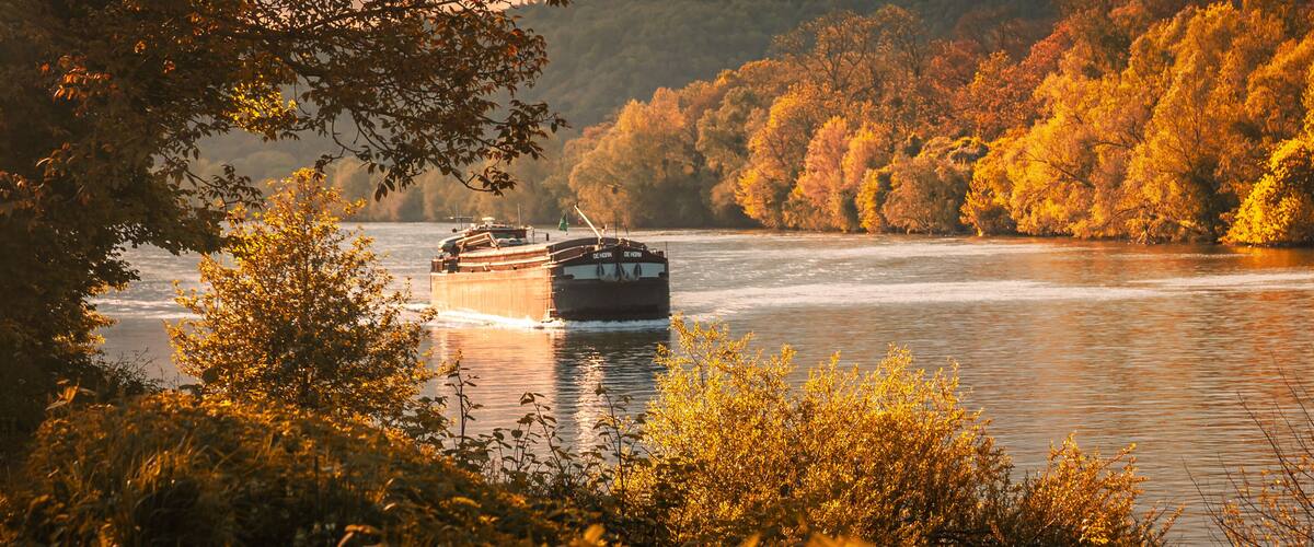 A riverboat on a river surrounded by autumn-colored trees.