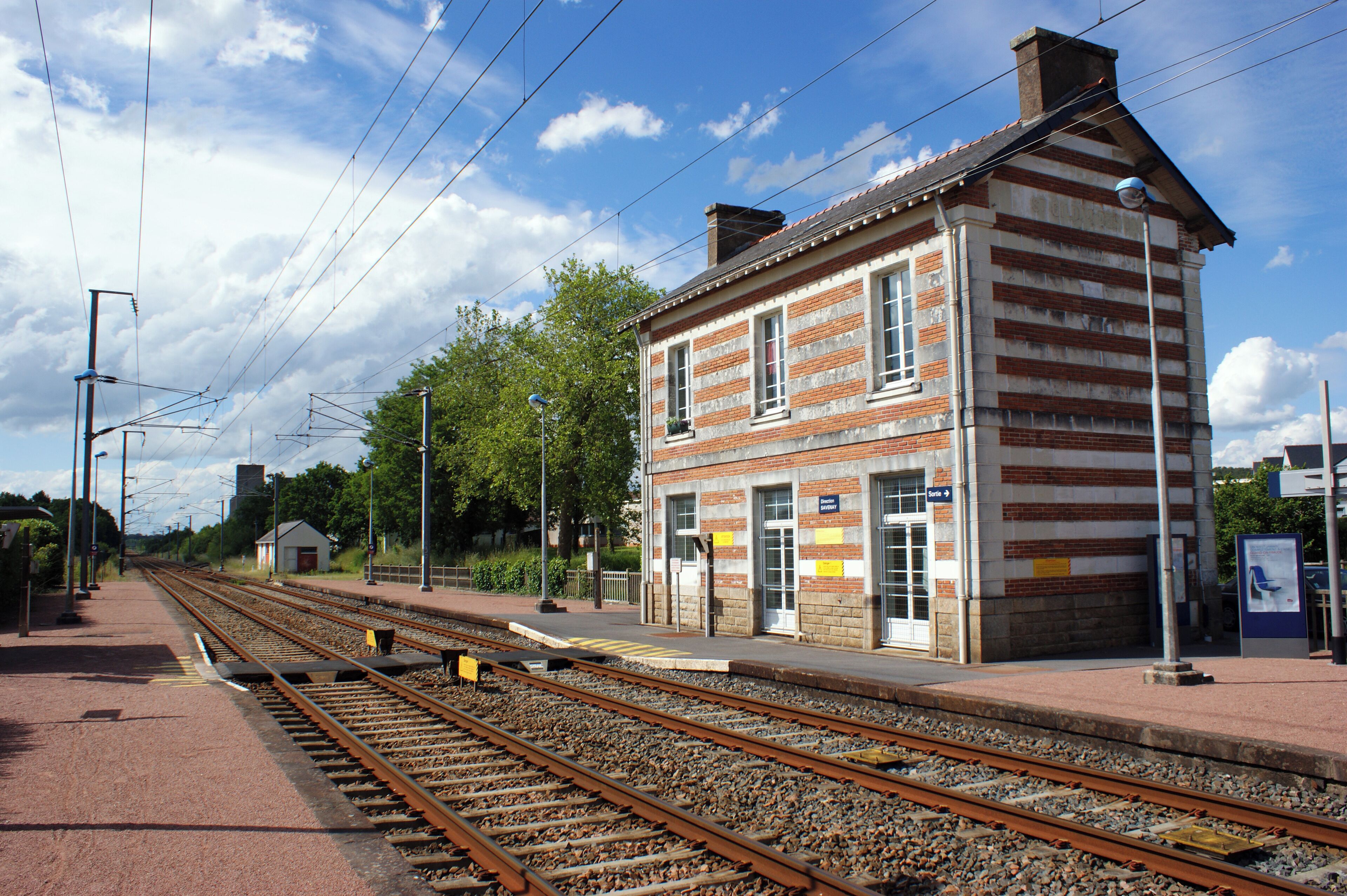 A railway station with a brick building, tracks, and a clear sky.