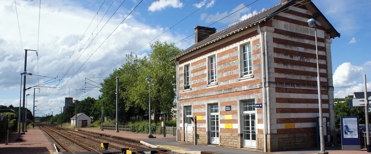 A railway station with a brick building, tracks, and a clear sky.