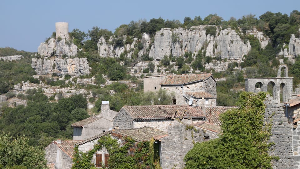 A village with stone buildings, a tower, and rocky cliffs.