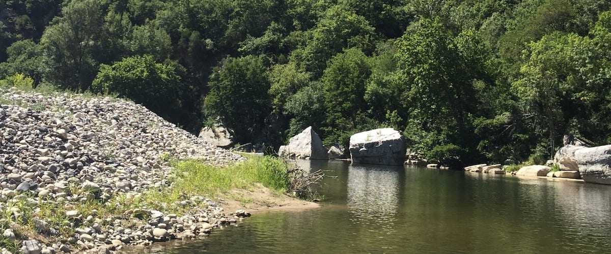 A river with clear water, surrounded by rocky terrain and dense green forest.
