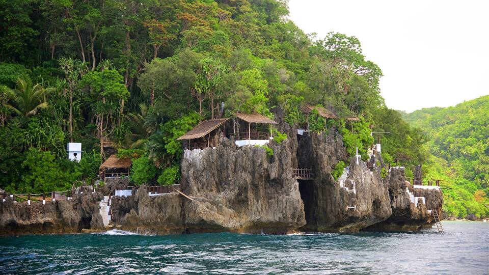 A rocky coastal landscape with lush greenery and traditional thatched-roof structures perched on the cliffs.