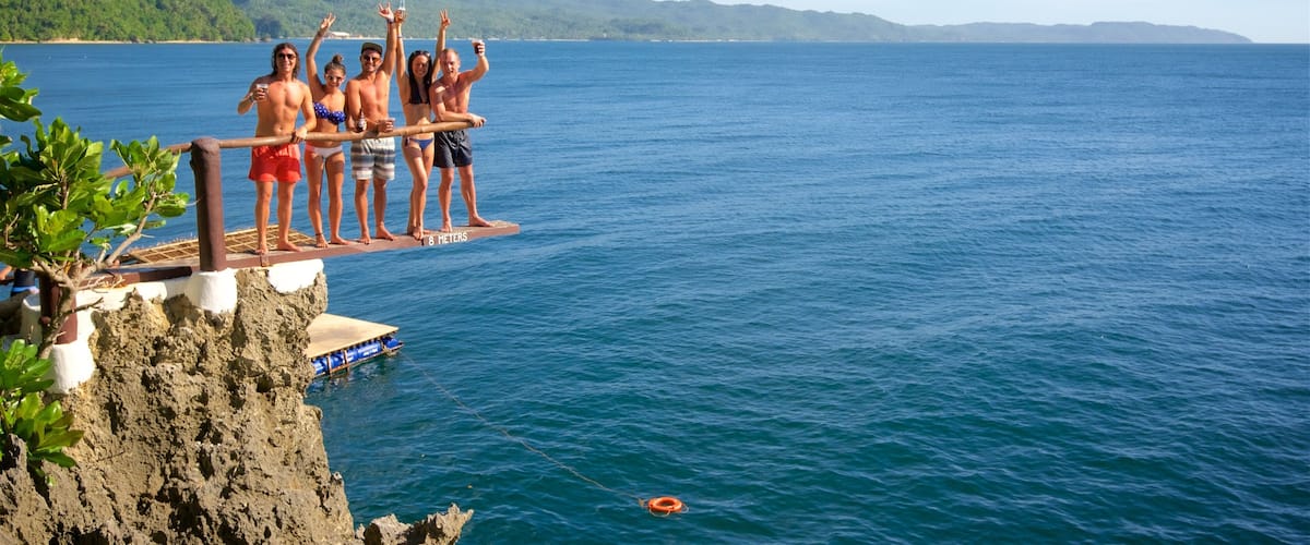 A group of people standing on a diving board over a body of water, with a boat visible in the background.