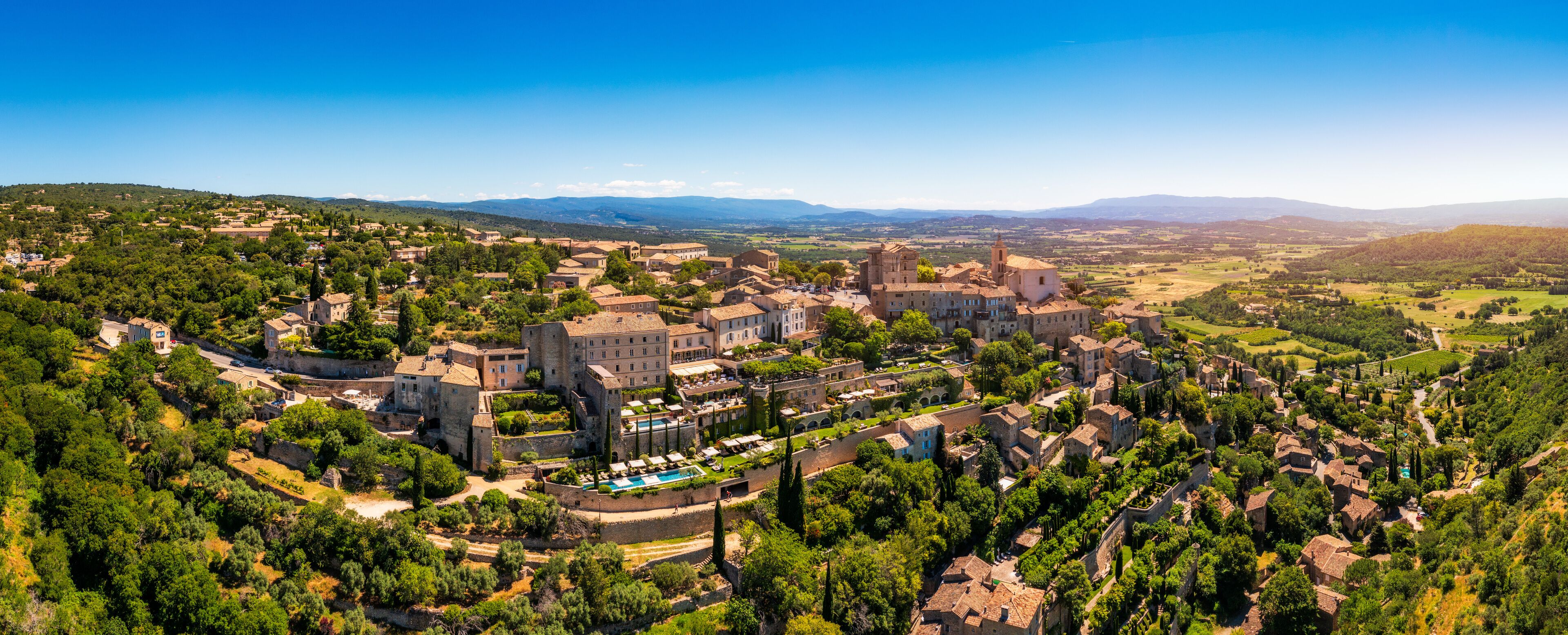 A historic town with medieval architecture, surrounded by lush greenery and rolling hills.