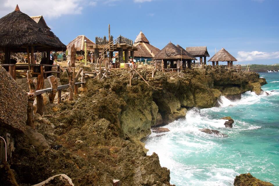 A coastal village with thatched-roof huts on rocky cliffs overlooking turquoise waters.
