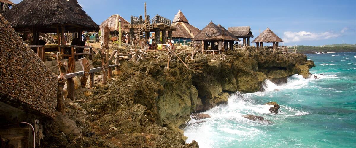 A coastal village with thatched-roof huts on rocky cliffs overlooking turquoise waters.