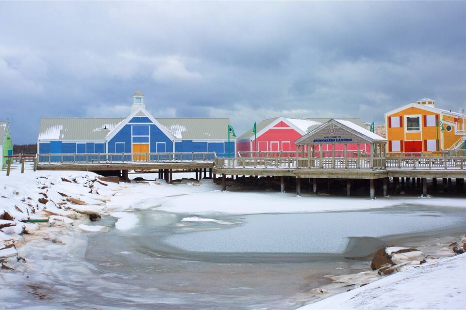 A pier with colorful buildings, a snowy landscape, and a frozen body of water.